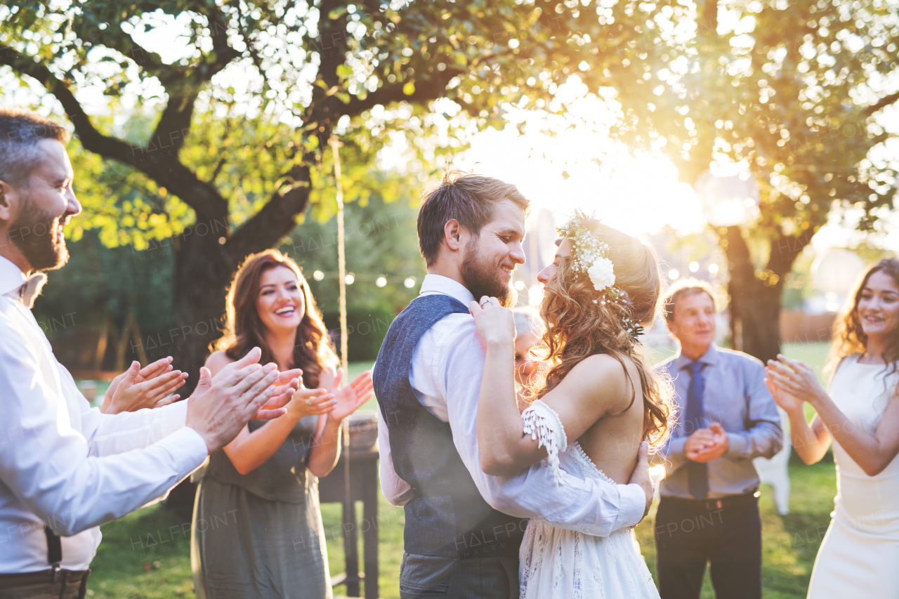 Wedding reception outside in the backyard. Bride and groom with a family dancing.