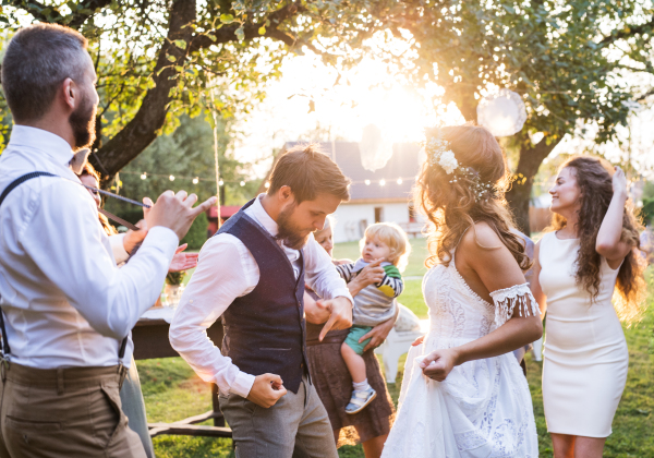 Wedding reception outside in the backyard. Bride and groom with a family dancing.