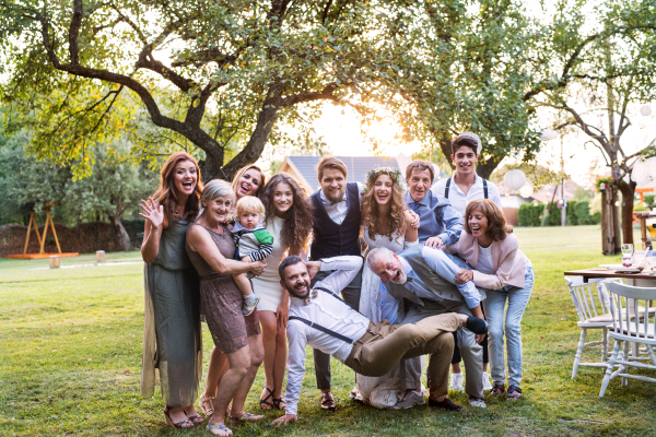 Wedding reception outside in the backyard. Family celebration. Bride, groom and their guests posing for the photo.