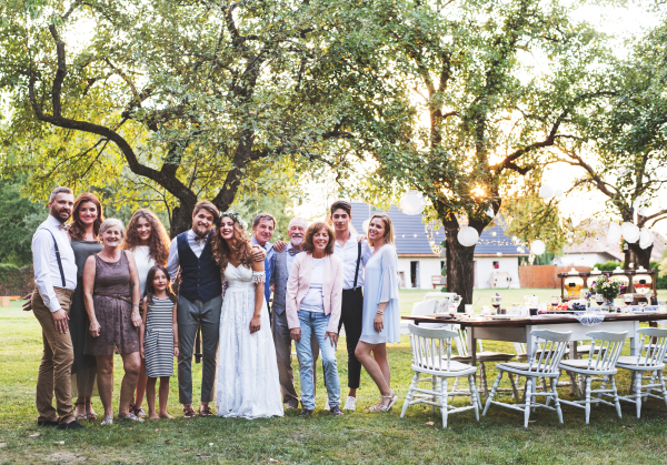 Wedding reception outside in the backyard. Family celebration. Bride, groom and their guests posing for the photo.