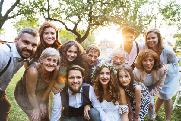 Wedding reception outside in the backyard. Family celebration. Bride, groom and their guests posing for the photo.