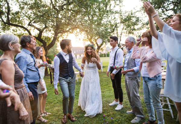 Bride, groom and their guests at the wedding reception outside in the backyard. Family celebration.