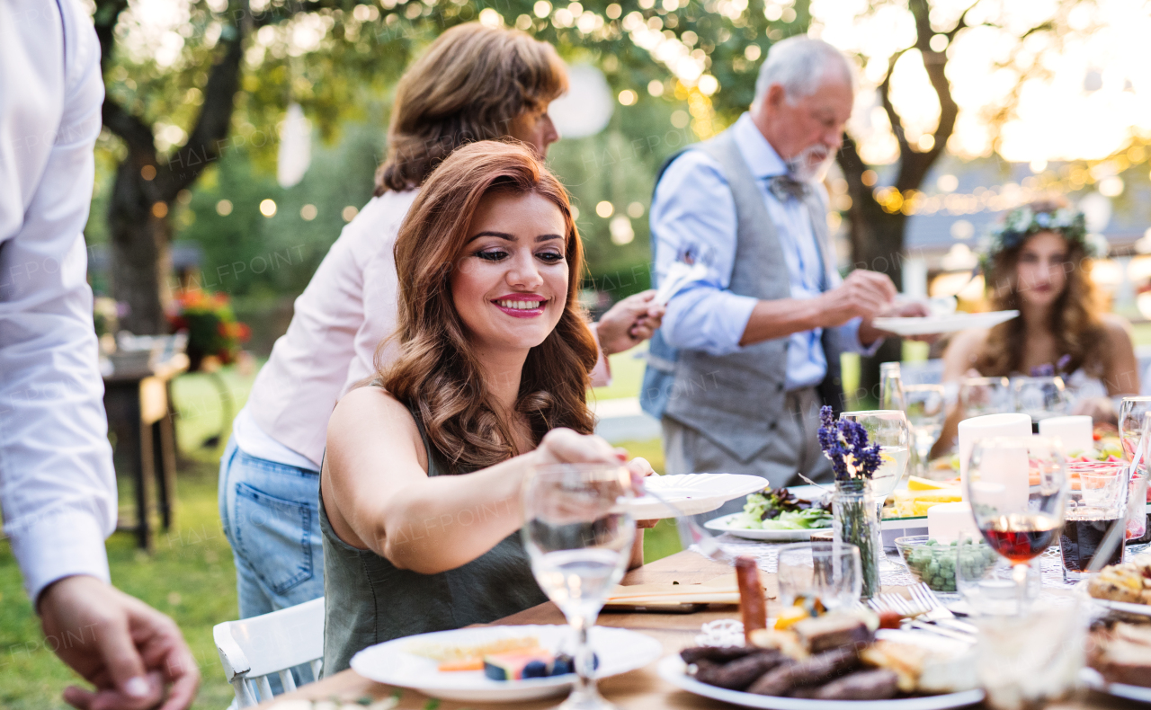 Guests sitting at the table and eating at the wedding reception outside in the backyard.