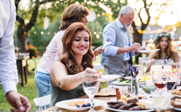 Guests sitting at the table and eating at the wedding reception outside in the backyard.