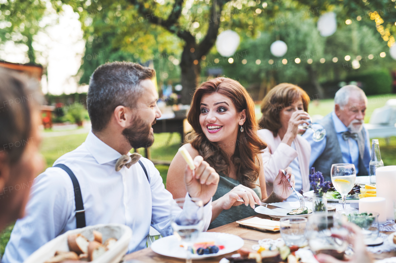 Guests sitting at the table and eating at the wedding reception outside in the backyard.