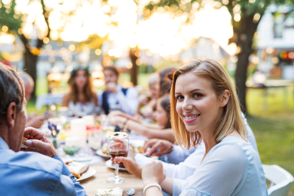 Wedding reception outside in the backyard. Bride, groom and the guests sitting at the table.