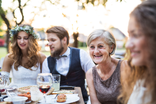 Wedding reception outside in the backyard. Bride, groom and the guests sitting at the table.