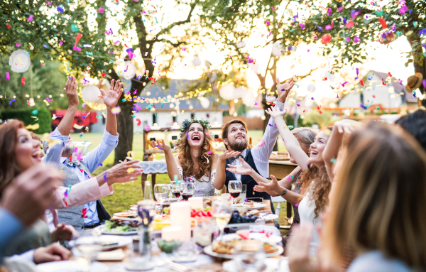 Wedding reception outside in the backyard. Bride and groom with family and guests sitting around the table, having fun.