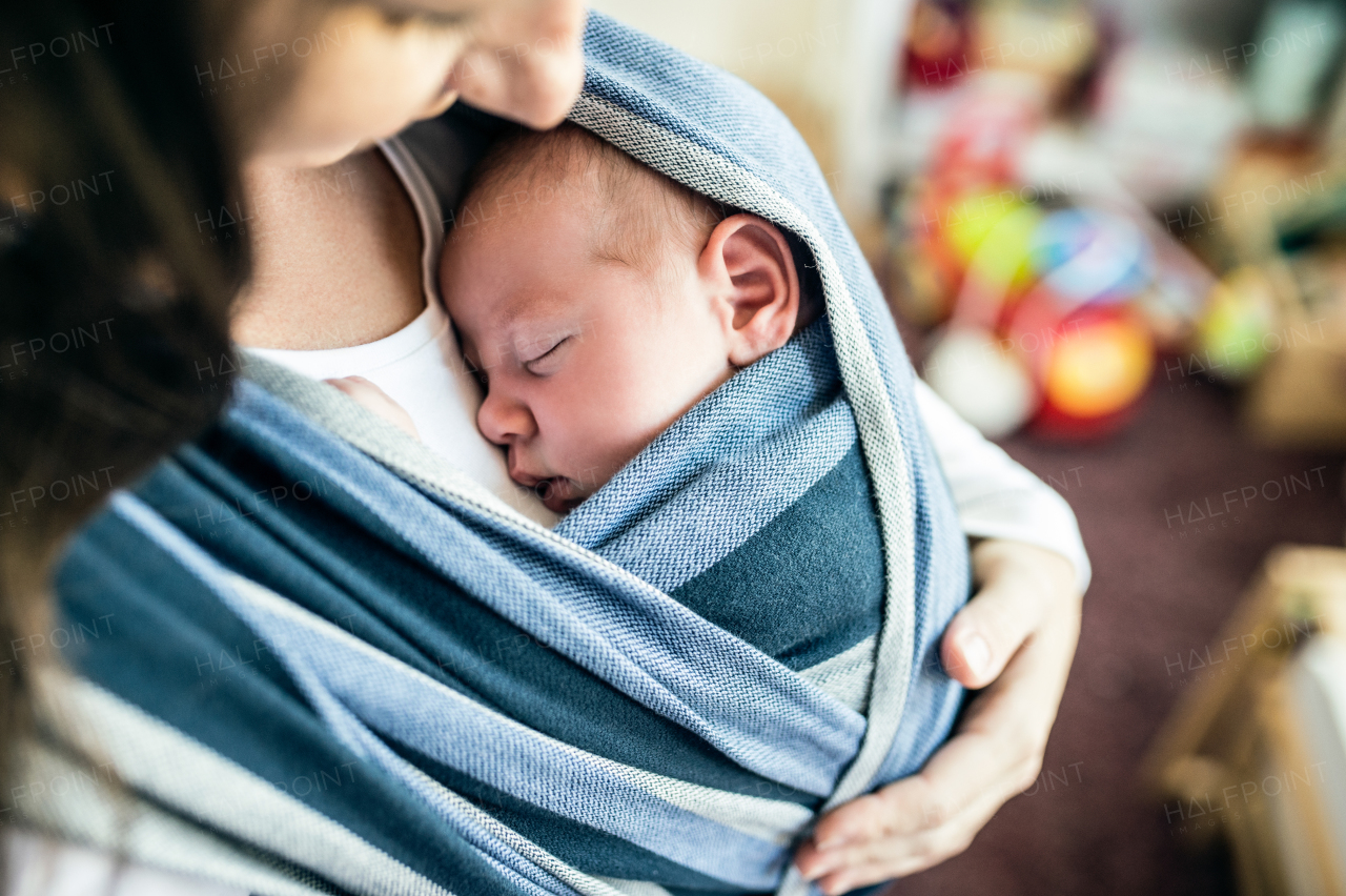 Close up of unrecognizable young mother with her newborn baby son in sling at home