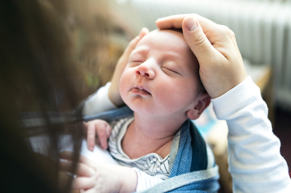 Close up of unrecognizable young mother with her newborn baby son in sling at home