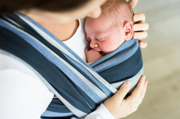 Close up of unrecognizable young mother with her newborn baby son in sling at home