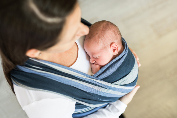 Close up of unrecognizable young mother with her newborn baby son in sling at home