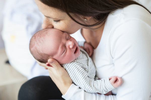 Beautiful young mother with her newborn baby son, sitting on bed in bedroom