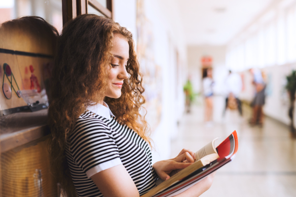 Attractive teenage girl with notebooks in high school hall during break.