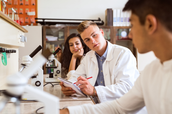 Group of high school student with microscopes in laboratory during biology class.