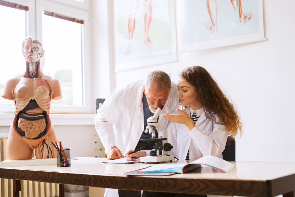 Senior teacher teaching biology to his high school student in laboratory. Human anatomy model.