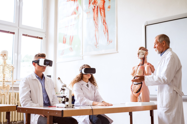 Senior teacher teaching biology to his high school students with virtual reality glasses in laboratory. Human anatomy model.