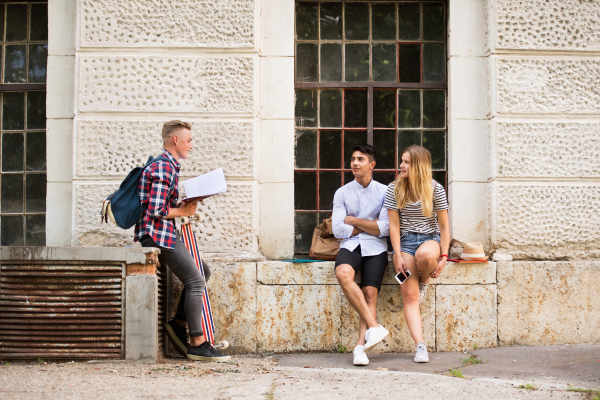 Group of attractive teenage students in front of university studying, talking together.