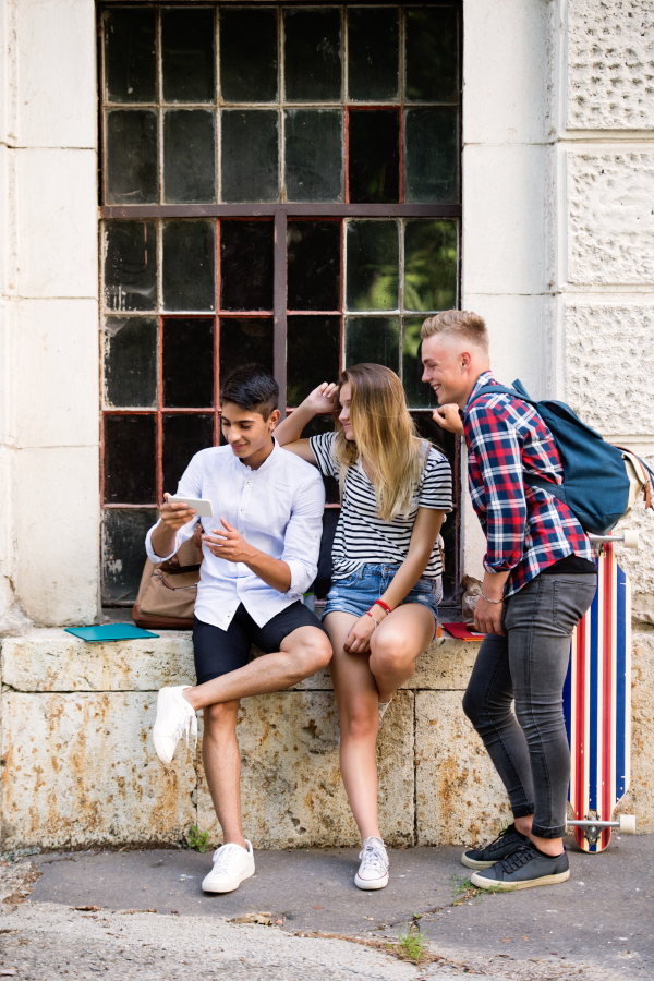 Group of attractive teenage students in front of university with smart phone, watching or reading something.