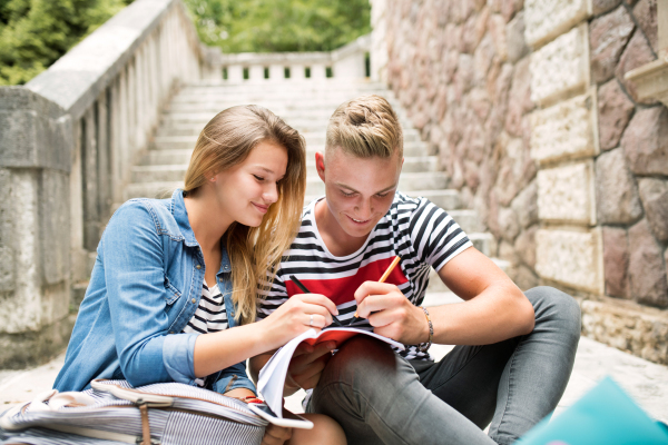 Attractive teenage student couple in front of university studying together.