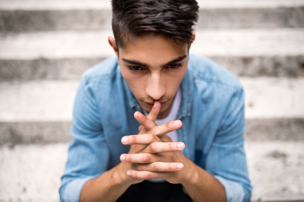 Handsome hispanic teenage student in denim shirt sitting on stone steps.