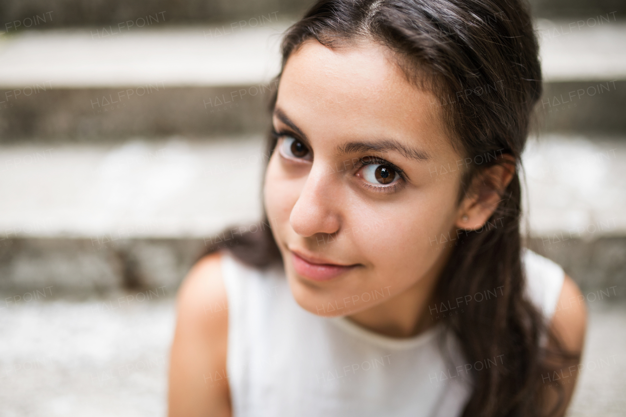 Face of attractive teenage student girl sitting on stone steps, smiling.