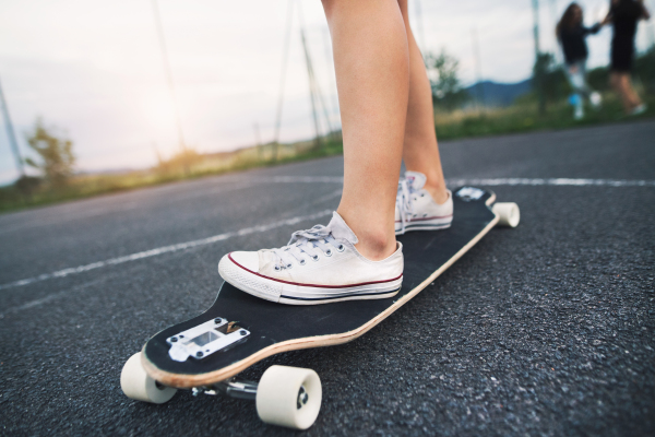 Close up of legs of unrecognizable teenage girl standing on skateboard outdoors on playground.