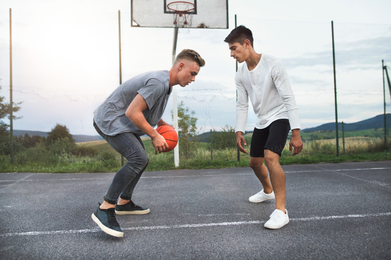 Two handsome teenage boys playing basketball outdoors on playground.