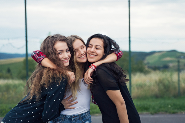 Three attractive teenage girls outdoors on playground hugging.