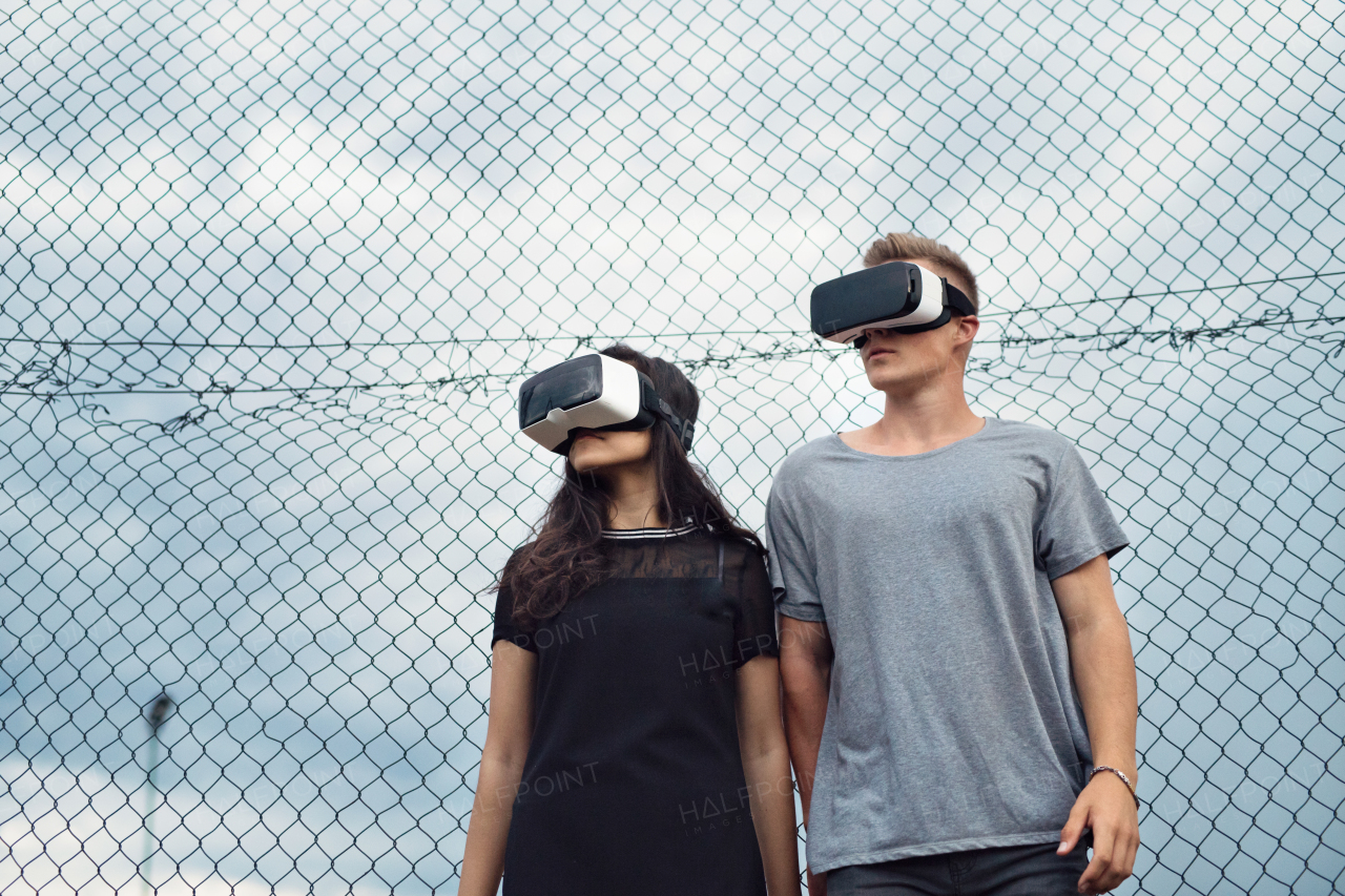 Attractive teenage couple outdoors on playground wearing virtual reality goggles.