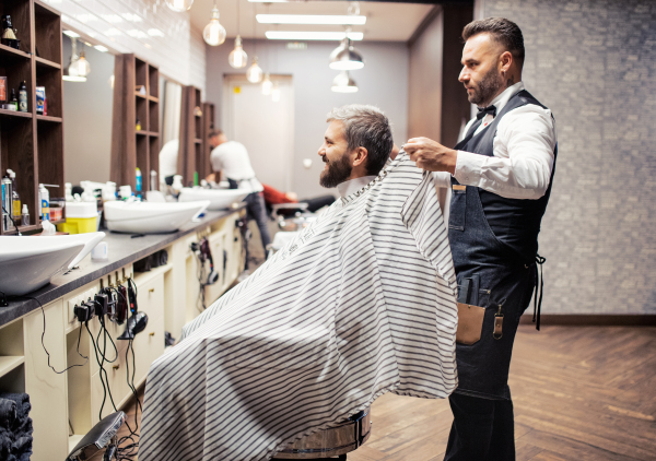 Handsome hipster man client visiting haidresser and hairstylist in barber shop.