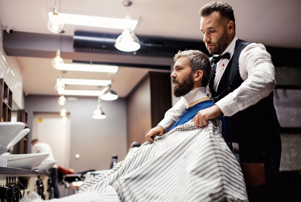 Handsome hipster man client visiting haidresser and hairstylist in barber shop.