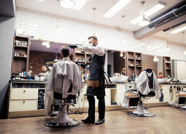 Handsome hipster man client visiting haidresser and hairstylist in barber shop.