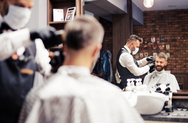 Handsome hipster man client visiting haidresser and hairstylist in barber shop.