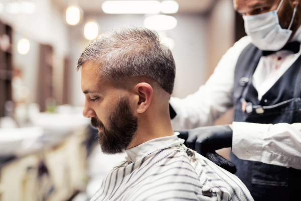 Handsome hipster man client visiting haidresser and hairstylist in barber shop.