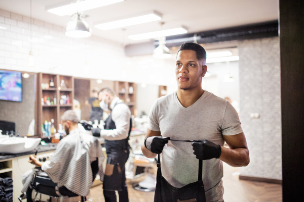 Young handsome hispanic haidresser and hairstylist standing in barber shop.