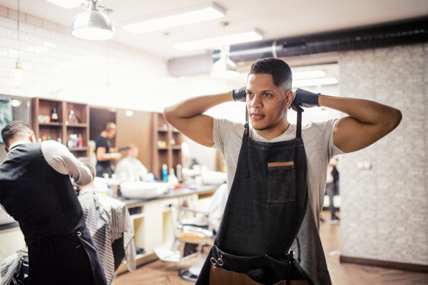 Young handsome hispanic haidresser and hairstylist standing in barber shop.