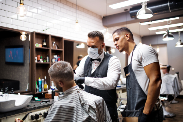 Handsome hipster man client visiting haidresser and hairstylist in barber shop, training concept.