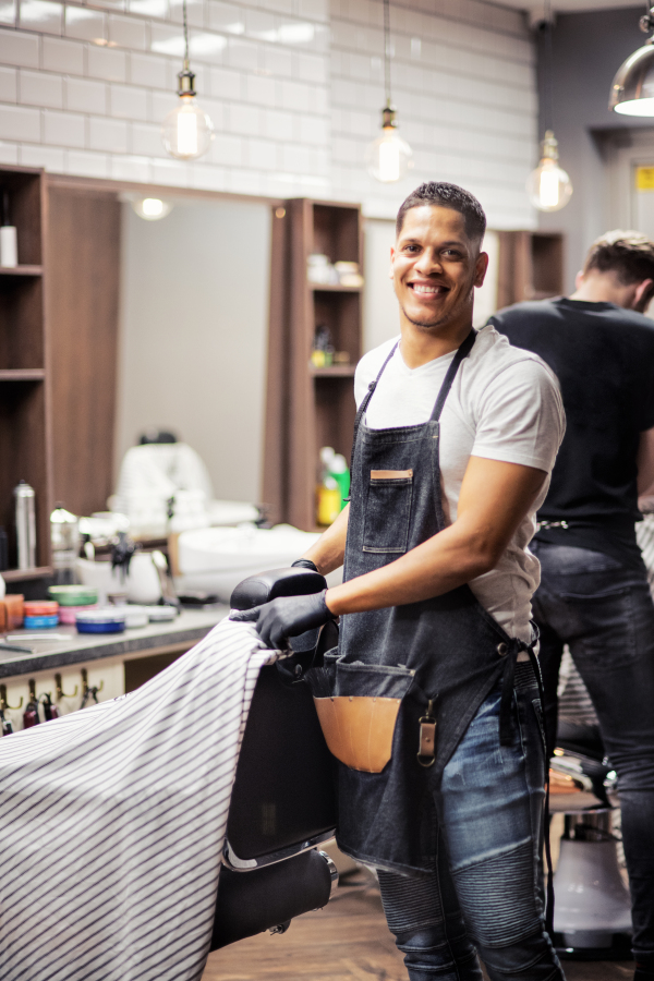 Young handsome hispanic haidresser and hairstylist standing in barber shop.