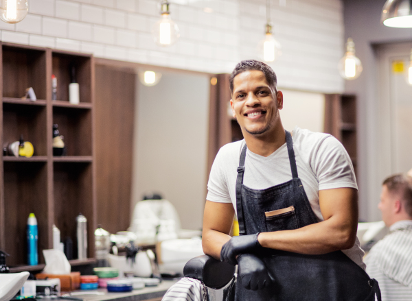 Young handsome hispanic haidresser and hairstylist standing in barber shop.