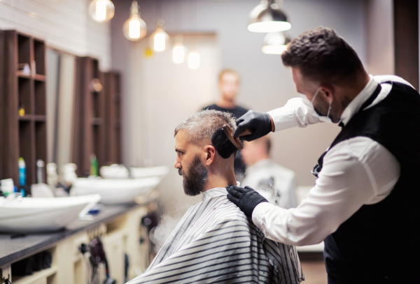 Handsome hipster man client visiting haidresser and hairstylist in barber shop.