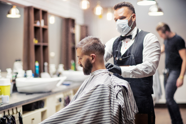 Handsome hipster man client visiting haidresser and hairstylist in barber shop.