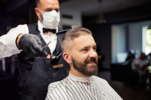 Handsome hipster man client visiting haidresser and hairstylist in barber shop.