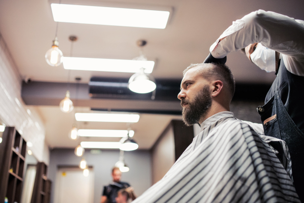 Handsome hipster man client visiting haidresser and hairstylist in barber shop.