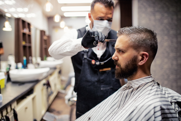 Handsome hipster man client visiting haidresser and hairstylist in barber shop.