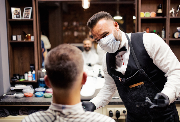 Handsome hipster man client visiting haidresser and hairstylist in barber shop.