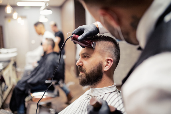 Handsome hipster man client visiting haidresser and hairstylist in barber shop.