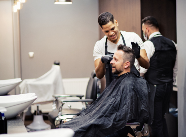 A hipster man client visiting haidresser and hairstylist in barber shop.