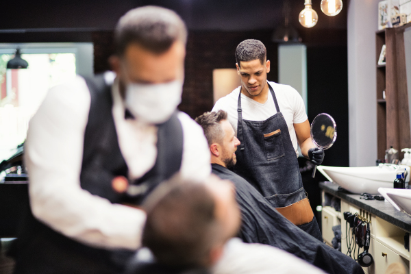 Two man clients visiting haidresser and hairstylist in barber shop.