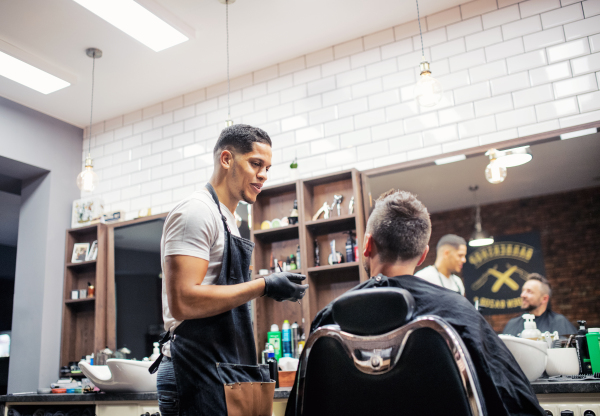 A mature man client talking to haidresser and hairstylist in barber shop.